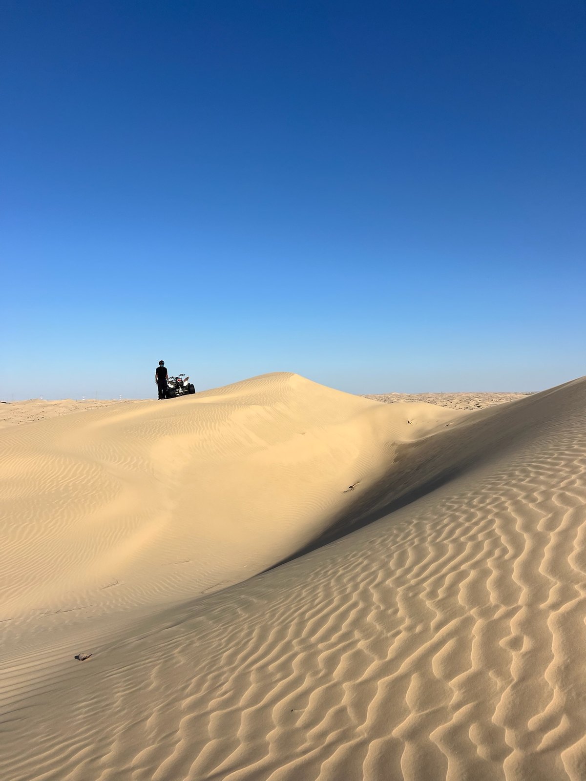 Lone rider on a quad bike paused atop a desert dune under a clear blue sky — build roots, not just routes